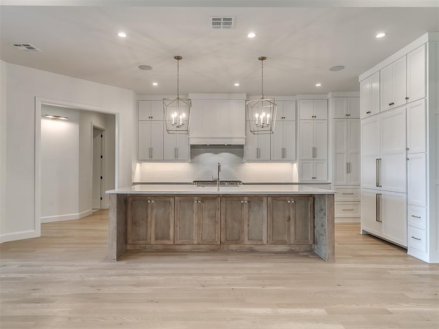 kitchen with decorative light fixtures, an island with sink, and white cabinets