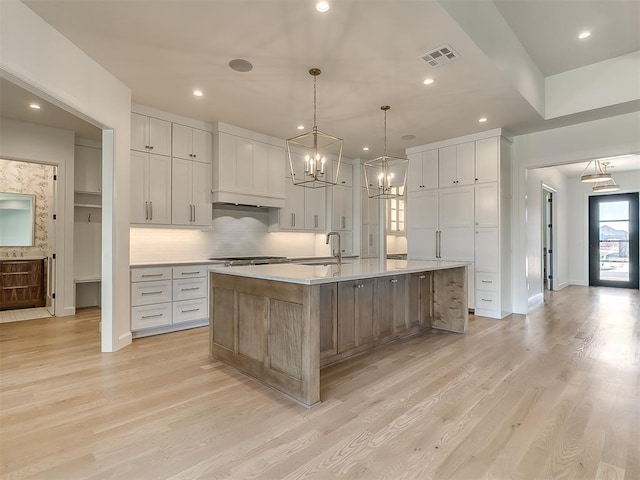 kitchen featuring sink, light hardwood / wood-style flooring, a spacious island, white cabinets, and decorative light fixtures