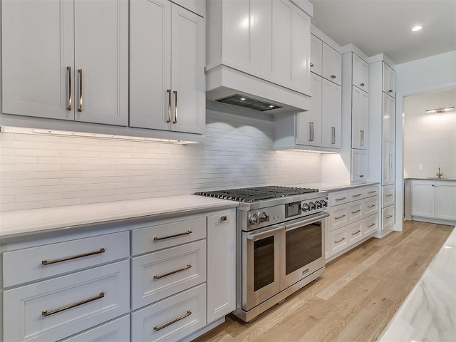 kitchen featuring light hardwood / wood-style flooring, premium range hood, white cabinetry, double oven range, and backsplash