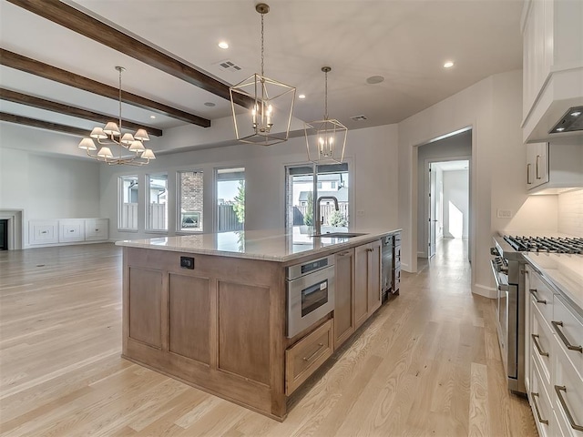 kitchen featuring white cabinets, hanging light fixtures, a kitchen island with sink, stainless steel appliances, and light stone countertops