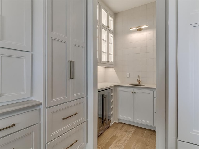 kitchen with sink, tasteful backsplash, wine cooler, light hardwood / wood-style floors, and white cabinets