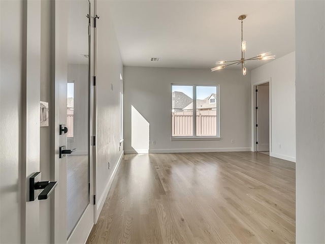 spare room featuring an inviting chandelier and light hardwood / wood-style flooring