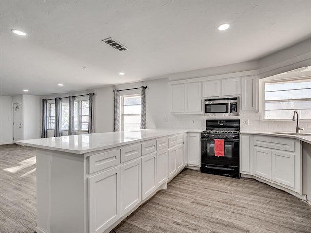 kitchen featuring white cabinetry, sink, black range with gas stovetop, kitchen peninsula, and light wood-type flooring