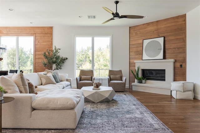 living room featuring dark hardwood / wood-style floors, ceiling fan, and wood walls