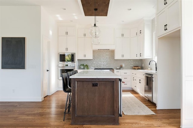 kitchen with appliances with stainless steel finishes, a kitchen island, pendant lighting, and wood-type flooring