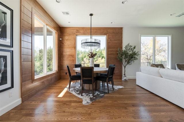 dining space with a notable chandelier, dark hardwood / wood-style floors, and wood walls