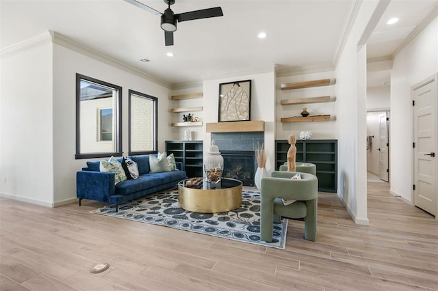 living room with ceiling fan, a tiled fireplace, crown molding, and light hardwood / wood-style flooring