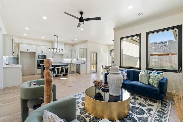 living room with ceiling fan, light wood-type flooring, and crown molding