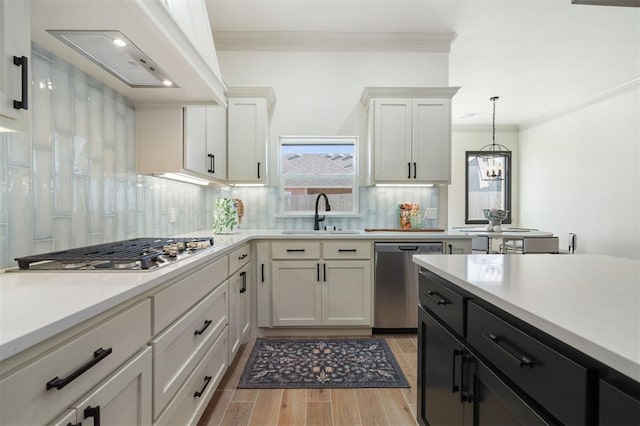 kitchen featuring appliances with stainless steel finishes, custom range hood, sink, decorative light fixtures, and white cabinetry