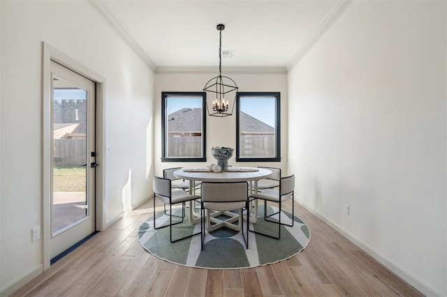 dining area with light wood-type flooring, crown molding, a wealth of natural light, and an inviting chandelier