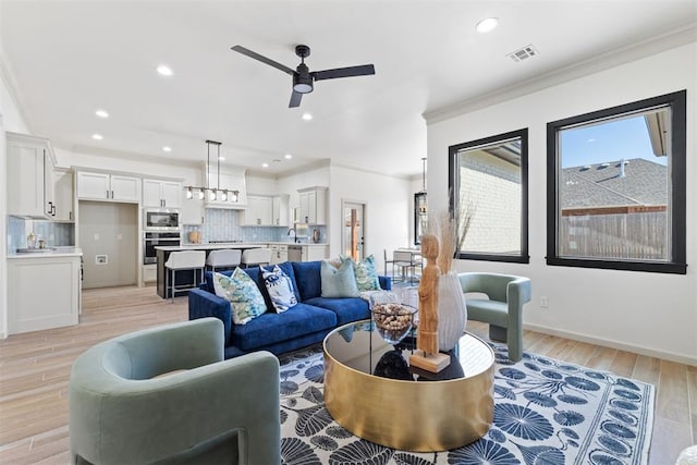 living area featuring crown molding, recessed lighting, visible vents, a ceiling fan, and light wood-type flooring