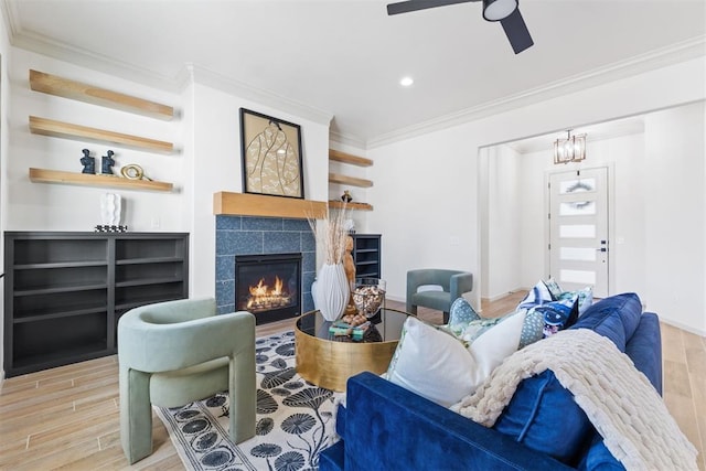 living area with crown molding, a tiled fireplace, ceiling fan, wood finished floors, and baseboards