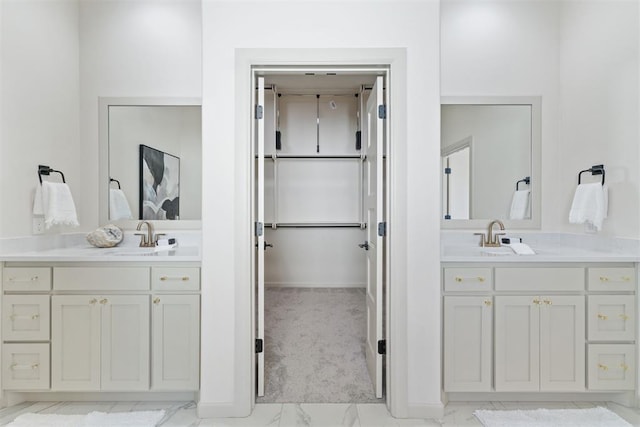 bathroom featuring marble finish floor, two vanities, a sink, and a walk in closet