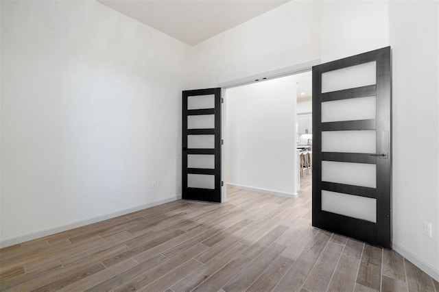 unfurnished room with a barn door, light wood-style flooring, and baseboards