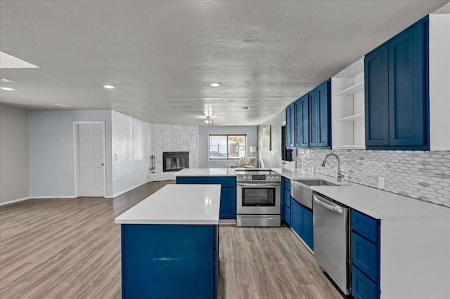 kitchen with kitchen peninsula, light wood-type flooring, stainless steel appliances, sink, and a stone fireplace