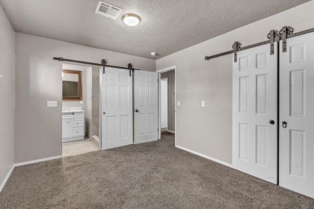 unfurnished bedroom featuring ensuite bathroom, a barn door, a textured ceiling, and a closet