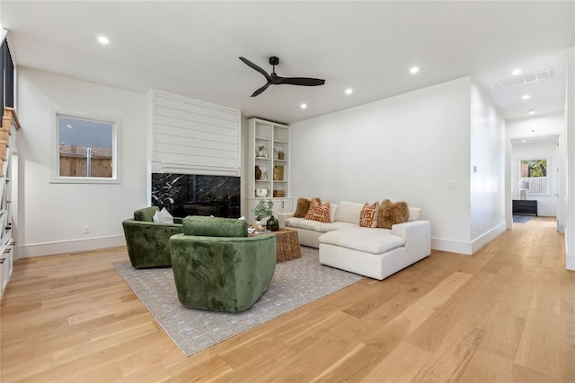 living room with a high end fireplace, light wood-type flooring, and ceiling fan