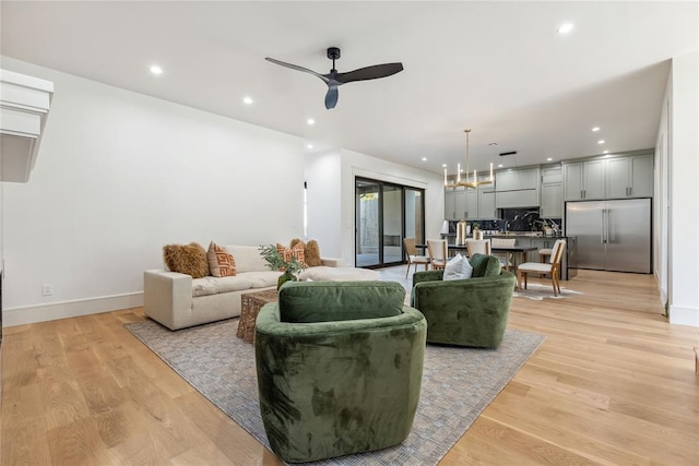 living room featuring ceiling fan with notable chandelier and light hardwood / wood-style floors