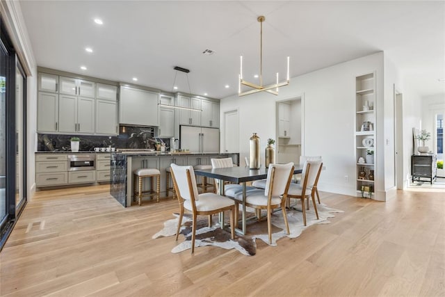 dining room with a chandelier, built in shelves, and light wood-type flooring