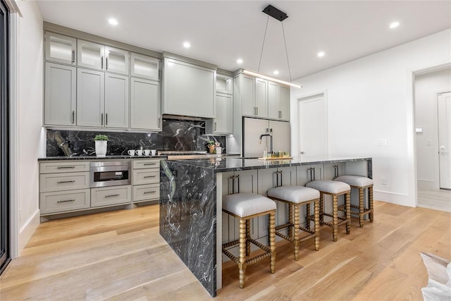 kitchen with a kitchen bar, pendant lighting, a center island with sink, light hardwood / wood-style flooring, and dark stone countertops