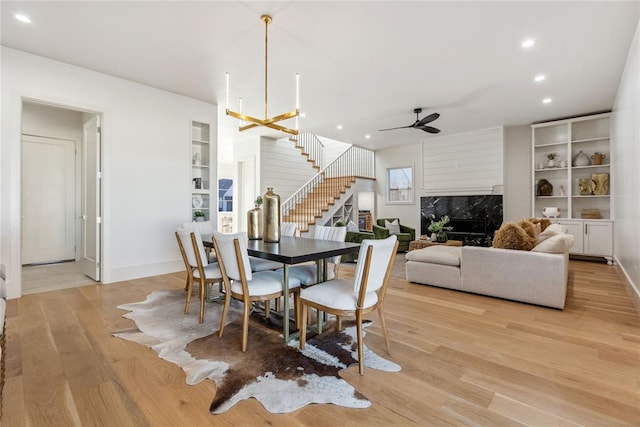 dining room featuring built in shelves, ceiling fan with notable chandelier, light hardwood / wood-style floors, and a premium fireplace