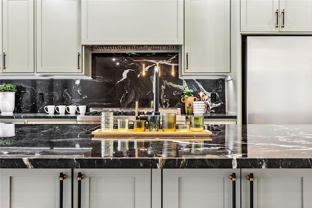 kitchen with decorative backsplash, dark stone countertops, and stainless steel refrigerator