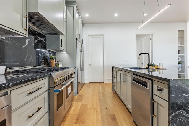 kitchen with gray cabinetry, stainless steel appliances, sink, dark stone countertops, and light hardwood / wood-style floors