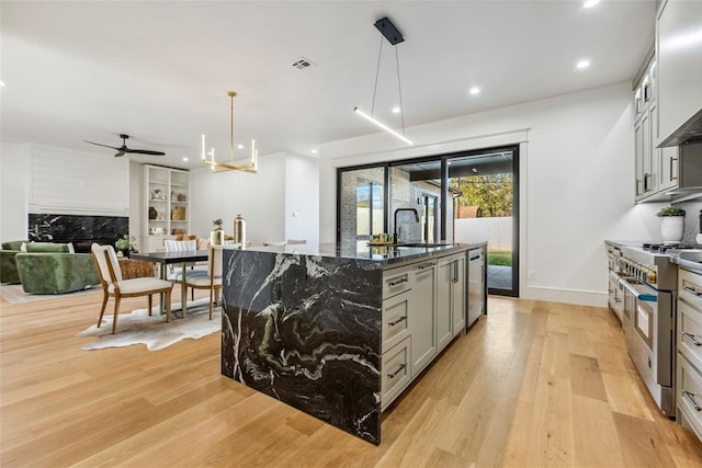 kitchen with decorative light fixtures, light hardwood / wood-style flooring, dark stone countertops, gray cabinets, and an island with sink