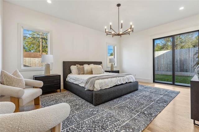 bedroom with access to outside, multiple windows, wood-type flooring, and an inviting chandelier