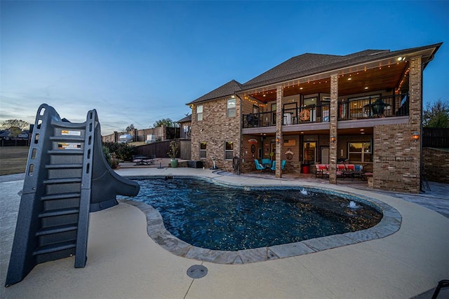 pool at dusk with a patio area and a water slide