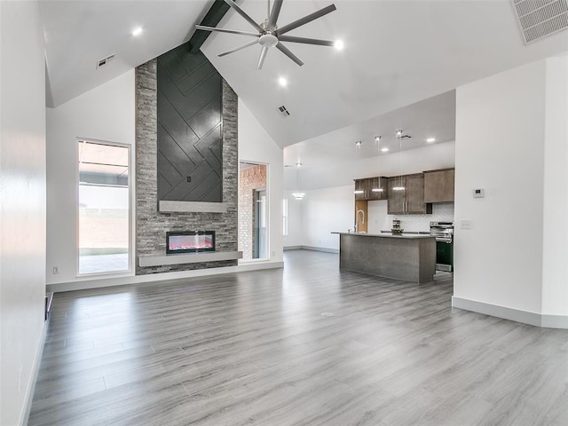 unfurnished living room with high vaulted ceiling, a stone fireplace, ceiling fan, beamed ceiling, and light hardwood / wood-style floors