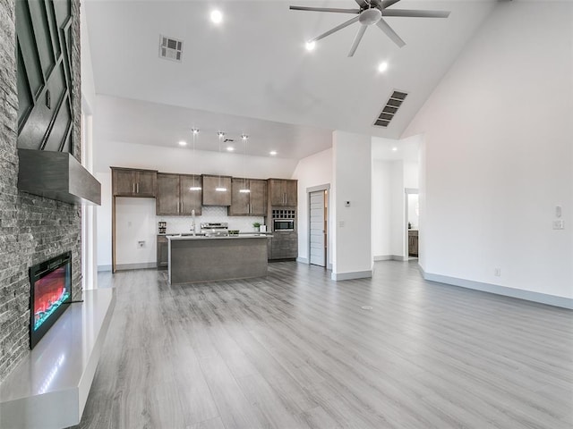 kitchen with high vaulted ceiling, light hardwood / wood-style flooring, ceiling fan, a fireplace, and an island with sink