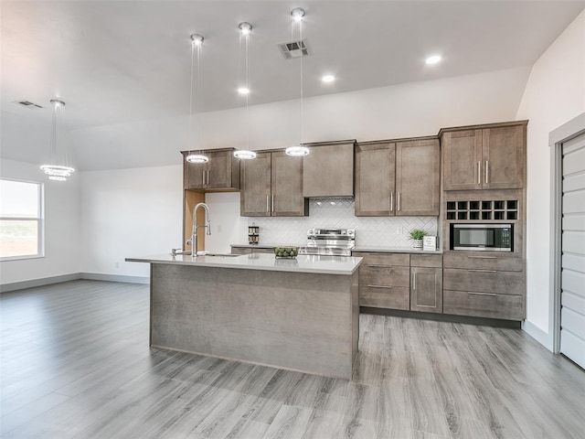 kitchen featuring a center island with sink, sink, light hardwood / wood-style flooring, appliances with stainless steel finishes, and decorative light fixtures