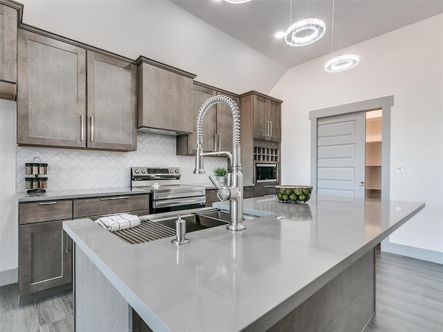 kitchen featuring hanging light fixtures, stainless steel appliances, wood-type flooring, vaulted ceiling, and a kitchen island with sink