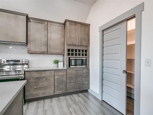 kitchen featuring decorative backsplash, stainless steel appliances, lofted ceiling, and light hardwood / wood-style floors