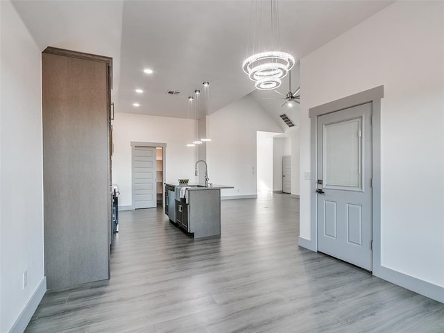 kitchen featuring light wood-type flooring, ceiling fan with notable chandelier, sink, decorative light fixtures, and a center island with sink