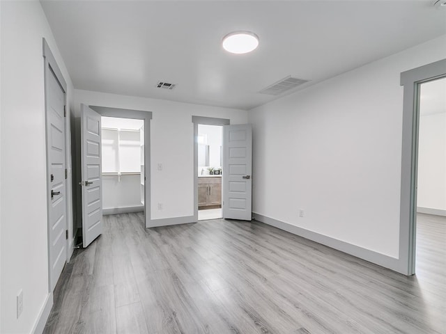 unfurnished bedroom with a closet, ensuite bath, a walk in closet, and light hardwood / wood-style flooring