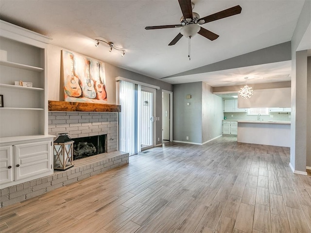 unfurnished living room with vaulted ceiling, ceiling fan, a brick fireplace, and light hardwood / wood-style floors