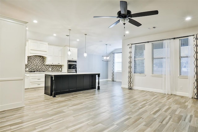 kitchen featuring decorative light fixtures, decorative backsplash, an island with sink, and white cabinets