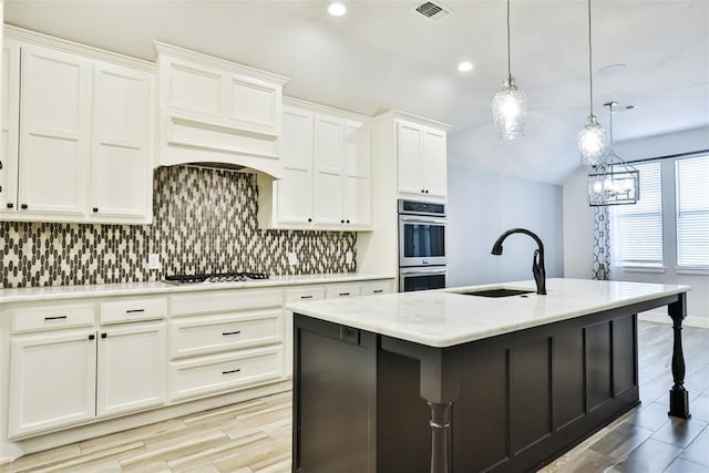 kitchen with sink, white cabinets, backsplash, hanging light fixtures, and a center island with sink