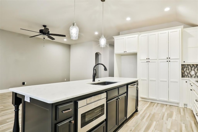 kitchen featuring sink, appliances with stainless steel finishes, a kitchen island with sink, white cabinetry, and decorative light fixtures