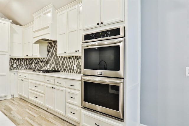 kitchen with vaulted ceiling, tasteful backsplash, white cabinetry, stainless steel appliances, and light wood-type flooring