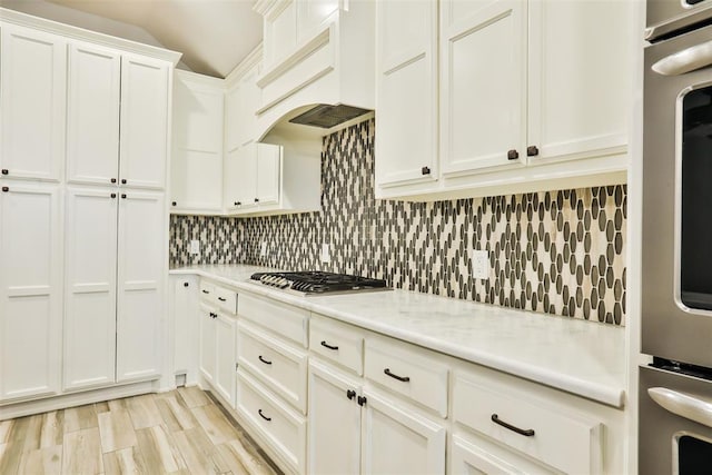 kitchen featuring stainless steel appliances, premium range hood, white cabinets, and decorative backsplash