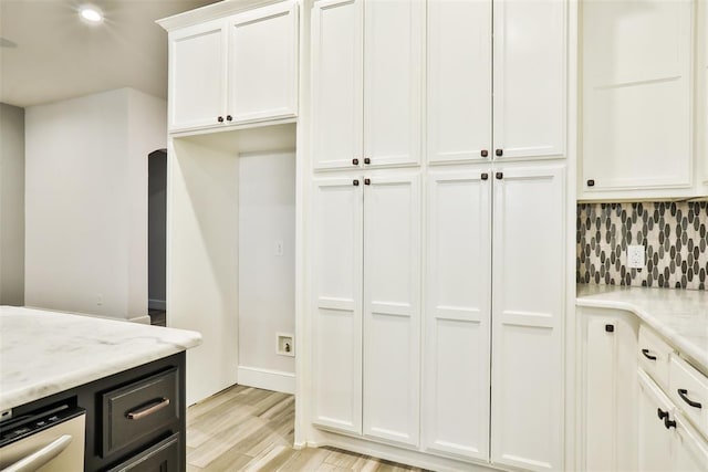 kitchen with tasteful backsplash, light stone countertops, white cabinets, and light hardwood / wood-style floors