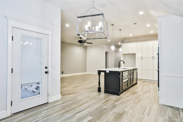 kitchen with ceiling fan with notable chandelier, white cabinetry, sink, hanging light fixtures, and a center island with sink