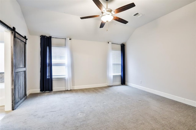 carpeted empty room with ceiling fan, a barn door, and vaulted ceiling