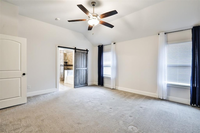 unfurnished bedroom featuring vaulted ceiling, a barn door, light colored carpet, and ceiling fan