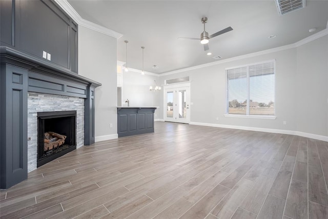 unfurnished living room with ceiling fan, french doors, a stone fireplace, crown molding, and light wood-type flooring