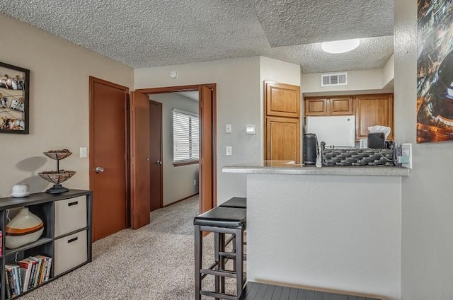 kitchen featuring a kitchen breakfast bar, a textured ceiling, white fridge, light colored carpet, and kitchen peninsula