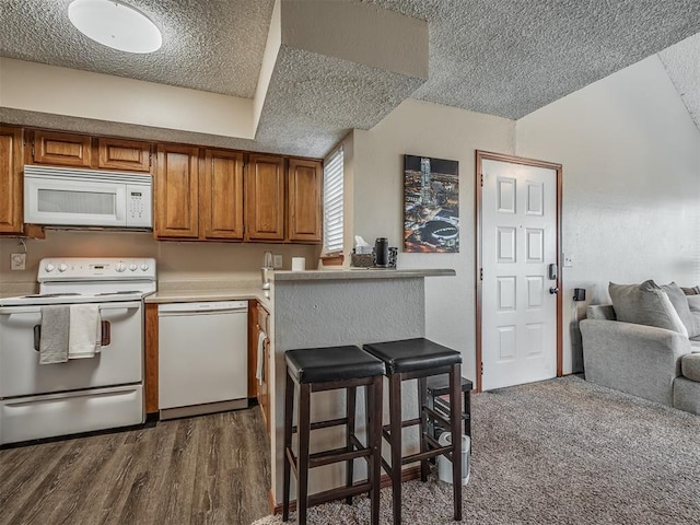 kitchen with a kitchen bar, a textured ceiling, white appliances, dark wood-type flooring, and lofted ceiling